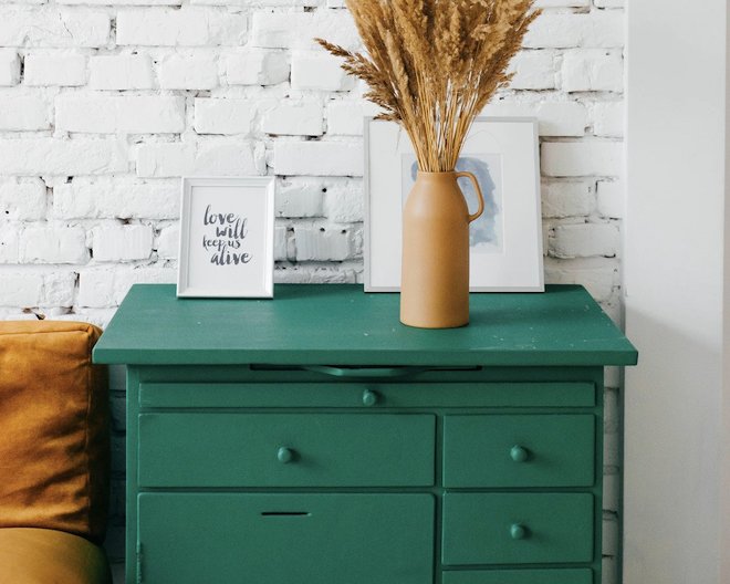 A vintage green drawer. On top of it is a vase and a few frames.